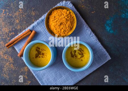 Flat lay Ayurvedic golden turmeric latte milk made with turmeric and other spices, on wooden background. Healthy medicine drink. Stock Photo