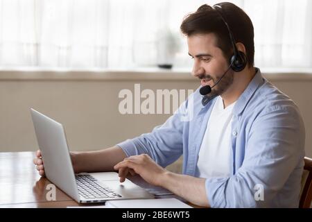 Young man wearing headset with microphone, looking at laptop screen. Stock Photo