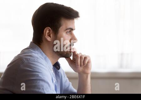 Distracted from job study young man touching chin, looking away. Stock Photo