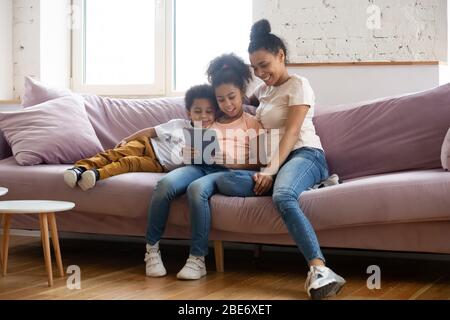 Happy african american mother looking at tablet screen with children. Stock Photo