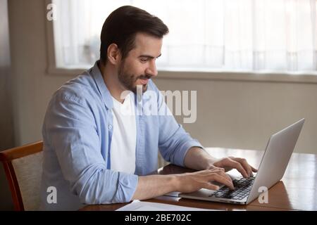 Handsome pleasant young man working remotely on computer at home. Stock Photo