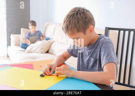 Boy making paper craft card with colored paper. Brother using tablet computer for online lesson at home Stock Photo