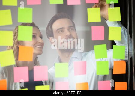 Smiling diverse colleagues write ideas on sticky notes Stock Photo