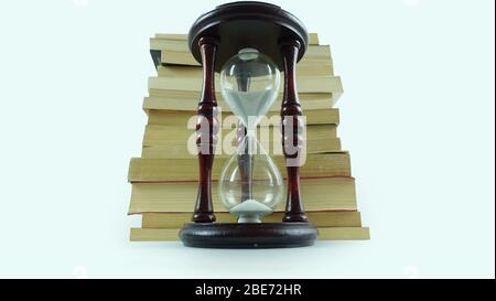 Hourglass placed in front of stacked books on a white background, symbolizing time, education, and knowledge. Stock Photo