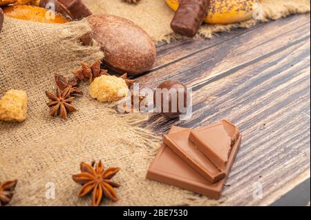 Chocolate, star anise, pieces of brown cane sugar and chocolate gingerbread on a background of fabric with a rough texture. Close up Stock Photo