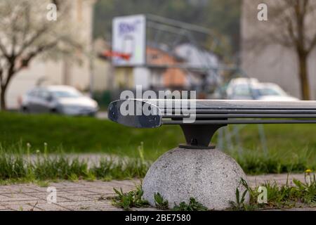 End of an empty bench in a city park in close up low angle with cars visible parked in the background in a concept of empty spaces due to the lockdown Stock Photo