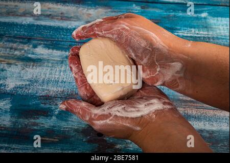 Someone is soaping their hands with a piece of toilet soap on a wooden background. Close up. Thorough hand washing with soap is a prevention of COVID- Stock Photo