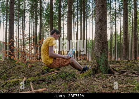 A man working with his laptop in a forest on the fresh air sitting on a trunk. Stock Photo