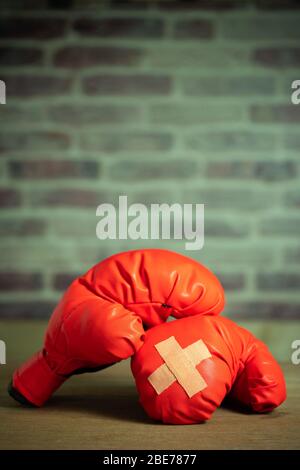 Red boxing gloves on wooden table and brick wall at the sport gym. Adhesive plaster across each other on boxing gloves. Idea of getting hurt or combat Stock Photo
