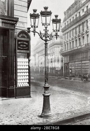 Place de l'Opéra. no. 4-  Oudry style lamp stand with three lamps on a street corner. Building immediately behind lamp stand has a plaque reading: WHR Cooke / And at London. 1878 Stock Photo