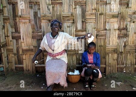 Smiling Dorze Tribe Woman seated in Front of a Bamboo Fence   demonstrating the Spinning of Wool Stock Photo
