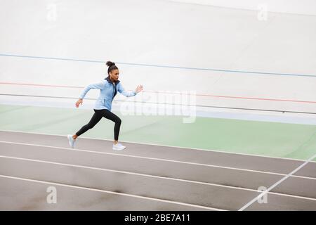 Beautiful young fit african sportswoman wearing wireless earphones running at the stadium Stock Photo