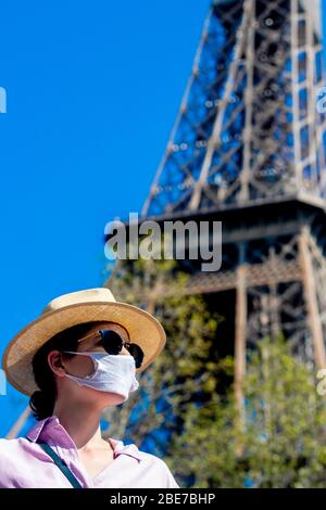 Paris, France. 12th Apr, 2020. A young French woman wearing a face mask as a preventive measure against the coronavirus, poses next to the Eiffel Tower during national lockdown. France will extend its nationwide lockdown put in place to contain the spread of the new coronavirus for a second time, meaning it will run beyond April 15. Credit: SOPA Images Limited/Alamy Live News Stock Photo