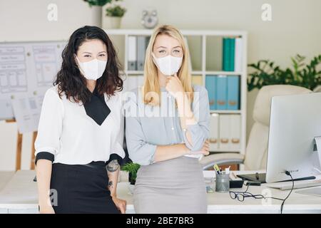 Portrait of positive multi-ethnic business team of women in medical masks working in office during coronavirus outbreak Stock Photo