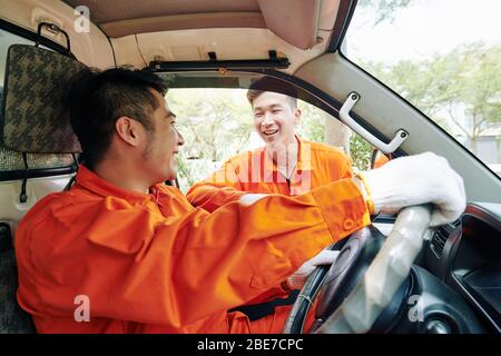 Smiling Vietnamese delivery service drivers in uniform having small talk before starting work Stock Photo
