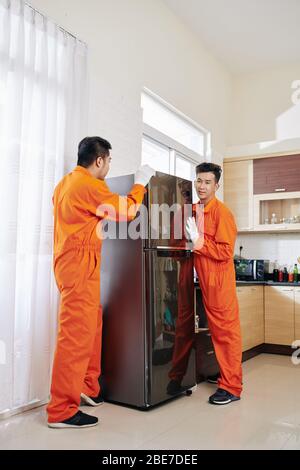 Team of movers in orange uniform deliverying fridge to house of customer Stock Photo