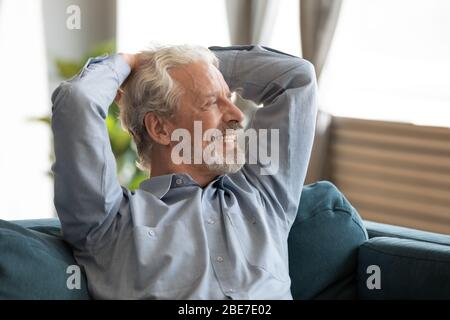 Smiling older man relaxing on couch, dreaming, looking into distance Stock Photo