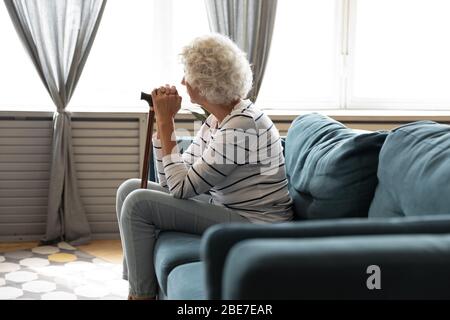 Rear view pensive older woman holding wooden cane Stock Photo