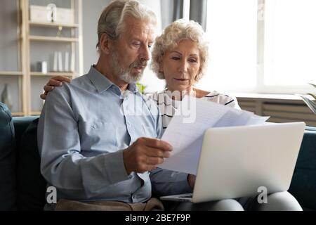 Serious older couple managing budget together, reading documents Stock Photo