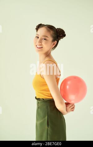 Adorable Asian girl holding a pink balloon while standing isolated on light background. Stock Photo