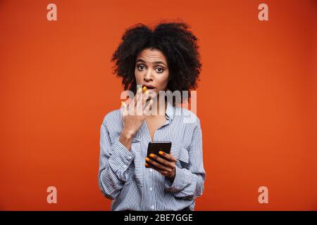 Confused young african woman using mobile phone isolated over red background Stock Photo