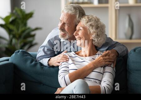Smiling older couple dreaming together, looking out window Stock Photo