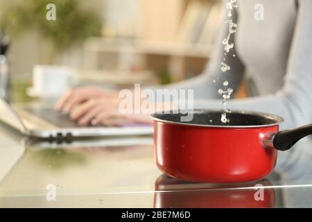 Close up of woman hands typing on laptop suffering water leaks falling on a pot on foreground sitting on a desk at home Stock Photo