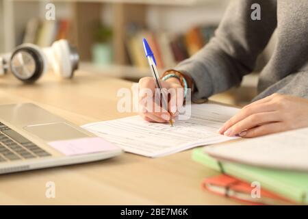 Close up of student girl hands filling out form document sitting on a desk at home