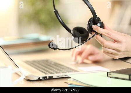 Close up of telemarketer holding headset working on laptop on a desk at home office Stock Photo