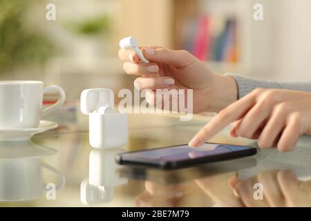 Close up of woman hands holding earbud checking smart phone on a desk at home Stock Photo