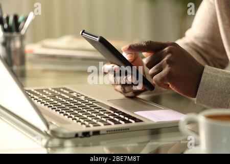 Close up of black man hands using smart phone with laptop at home Stock Photo