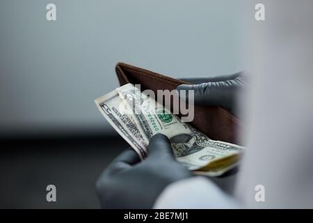 Man holding a wallet with  money dollars  in hand in black medical gloves. Coronavirus crisis. Save money. No maney.  The world crisis Stock Photo