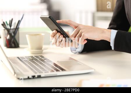 Close up of executive woman hands with laptop checking smart phone at the office Stock Photo
