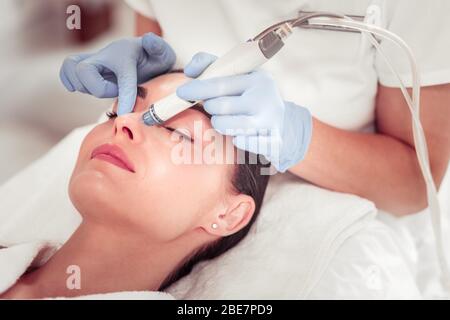 Using modern equipment. Cosmetologist wearing gloves using modern equipment for face cleansing Stock Photo