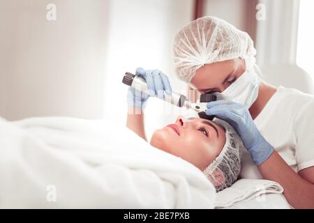 Examining the skin. Dermatologist wearing mask and gloves examining the skin of client before cleansing Stock Photo