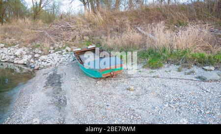 An old wooden fishing boat remained on the shore of the lake. An abandoned fishing boat on the bank of the Danube. A green boat left on a pebble bank.