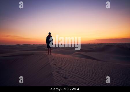 Lonely man standing on sand dune in the middle of desert at dusk. Abu Dhabi, United Arab Emirates Stock Photo
