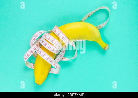 Banana with tape for measuring figure. Centimeter ruler spinned around fruit. Tape wrapped around banana isolated on mint background. Weight loss Stock Photo