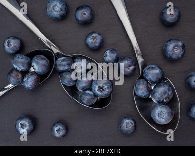 Looking down on a flat lat of blueberries in spoons on a slate background