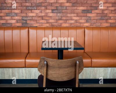 Furniture decoration in cafe retro style. Empty wood table bar and orange long leather sofa and wooden chair on brick wall background. Stock Photo