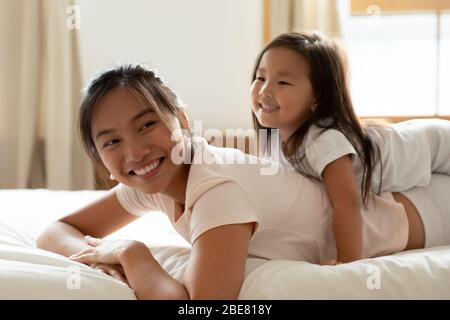 Little daughter and asian mother playing while lying on bed Stock Photo