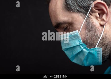 side portrait of a man with a medical mask and close eyes on a black background Stock Photo