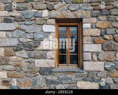 Old wooden window in a Hand-made natural stone building The wall is made of different size and shape stones. Flowers and flower pots are visible throu Stock Photo