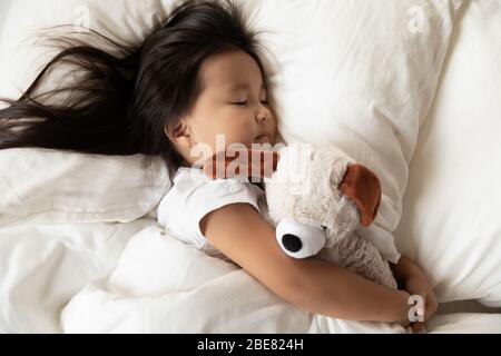 Asian little girl hugs plush toy sleeping in bed Stock Photo