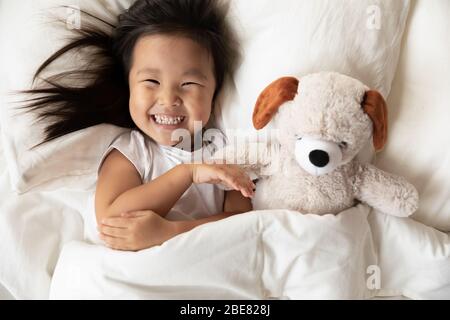 Asian little girl lying in bed with plush toy Stock Photo