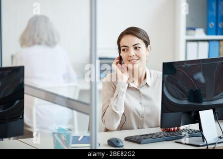 Portrait of smiling businesswoman wearing headset while working as call center operator in office interior, copy space Stock Photo
