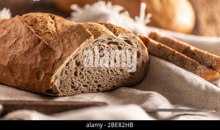 Two slices of freshly baked bread placed on top of the loaf and a linen cloth with a knife on a side. Stock Photo