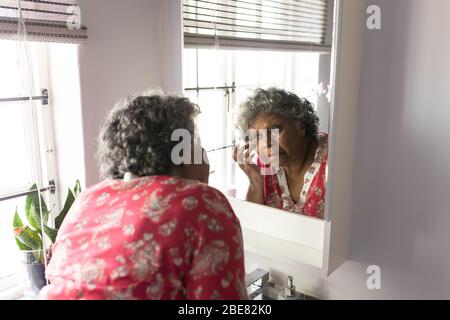 A senior African American woman looking at her reflexion in the mirror and taking care of herself Stock Photo