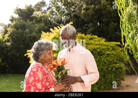 An African American man offering flowers to his wife, spending time together in the garden Stock Photo