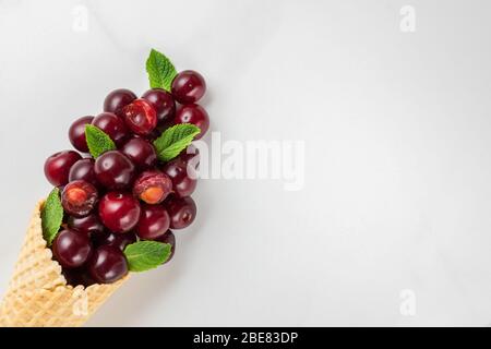 Fresh summer cherry berries with mint in waffle cone on white marble background. summer food concept. top view with copy space. flat lay Stock Photo